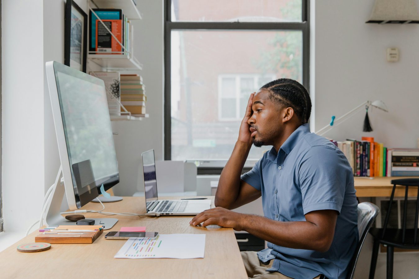man using a desktop computer, with one hand on his head, appearing disappointed