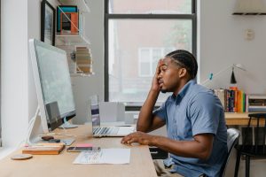 man using a desktop computer, with one hand on his head, appearing disappointed